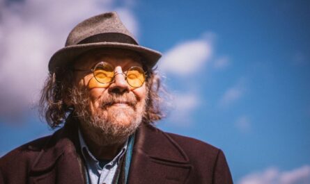 Bill Fay mit Hut und Brille vor einem blauen Himmel
