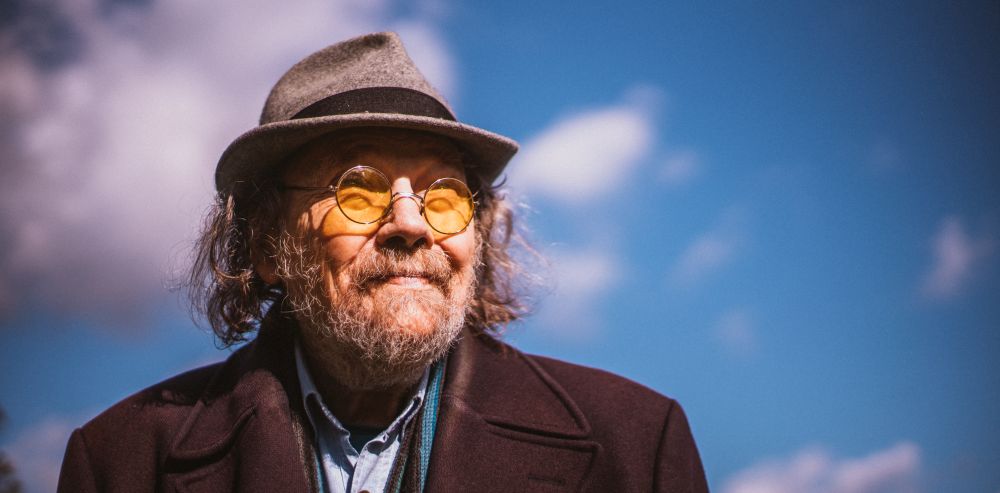 Bill Fay mit Hut und Brille vor einem blauen Himmel